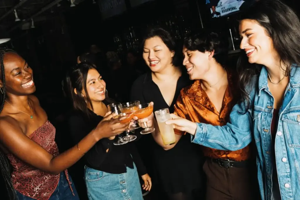 A group of friends laughing and making a toast with craft cocktails and beers during an interactive nightlife, and lively corporate group event at AceBounce in Chicago.