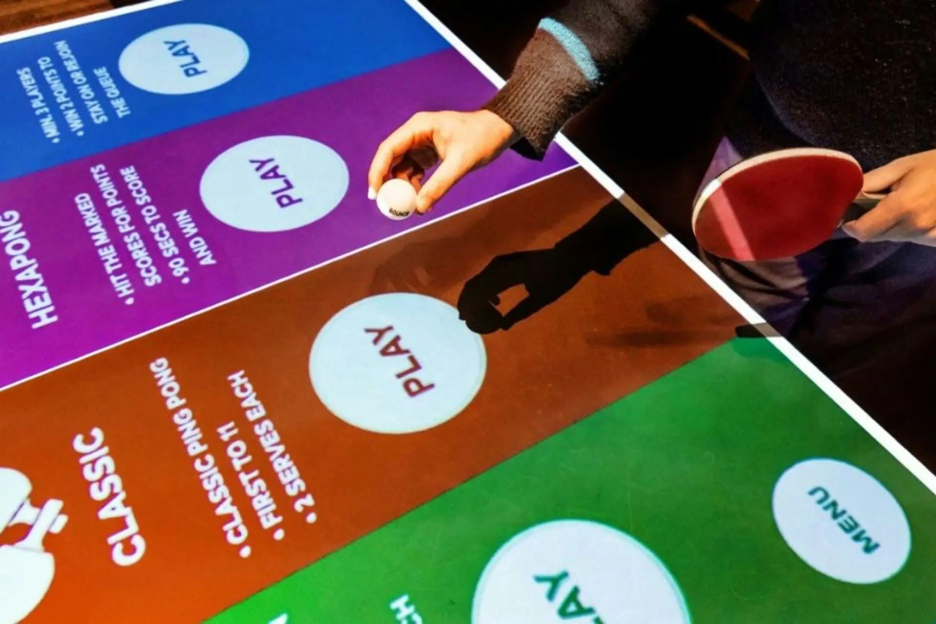 A player holding a paddle and ball at a high-tech interactive ping pong table, a popular team building activity for a corporate outing in Chicago Loop at AceBounce.